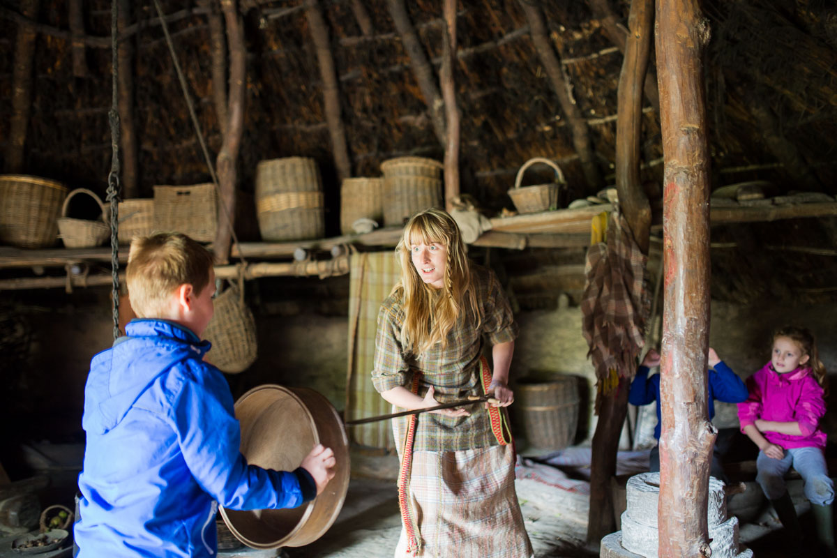 A costumed guide inside a roundhouse at Castell Henllys Iron Age Village is speaking to a young boy