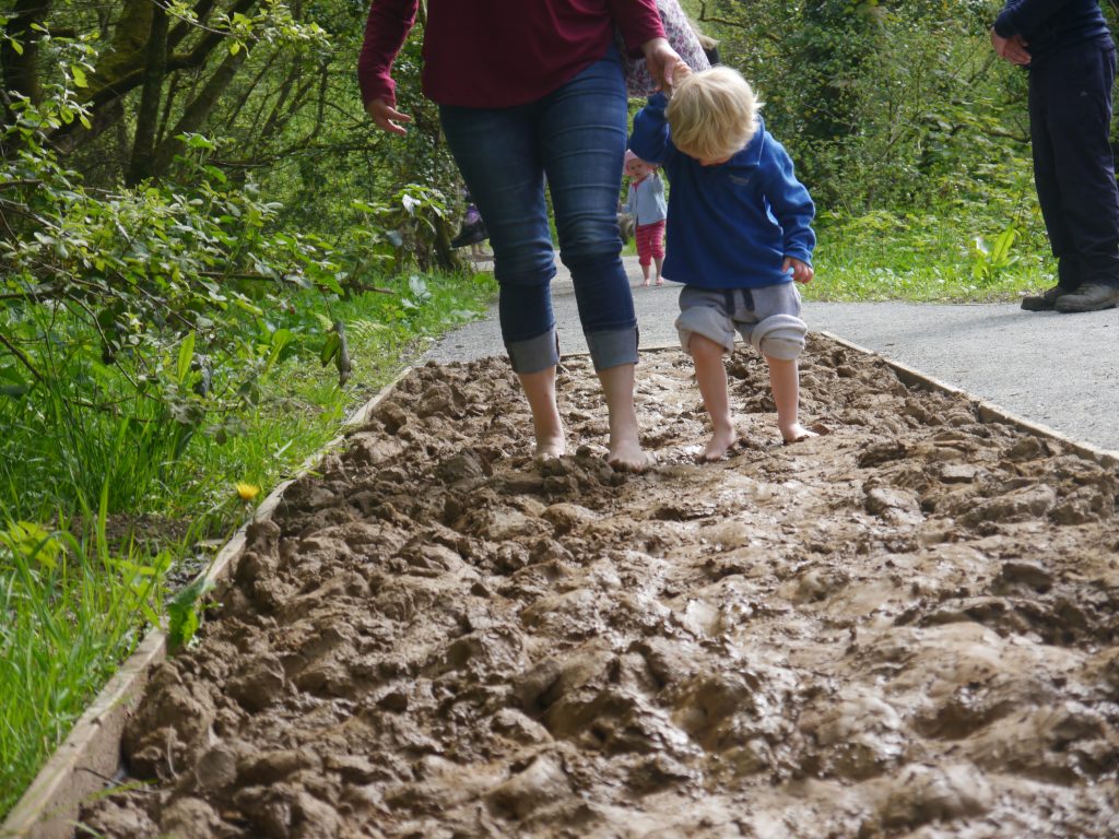 A mother and child walking barefoot in sand at the Barefoot Trail in Castell Henllys