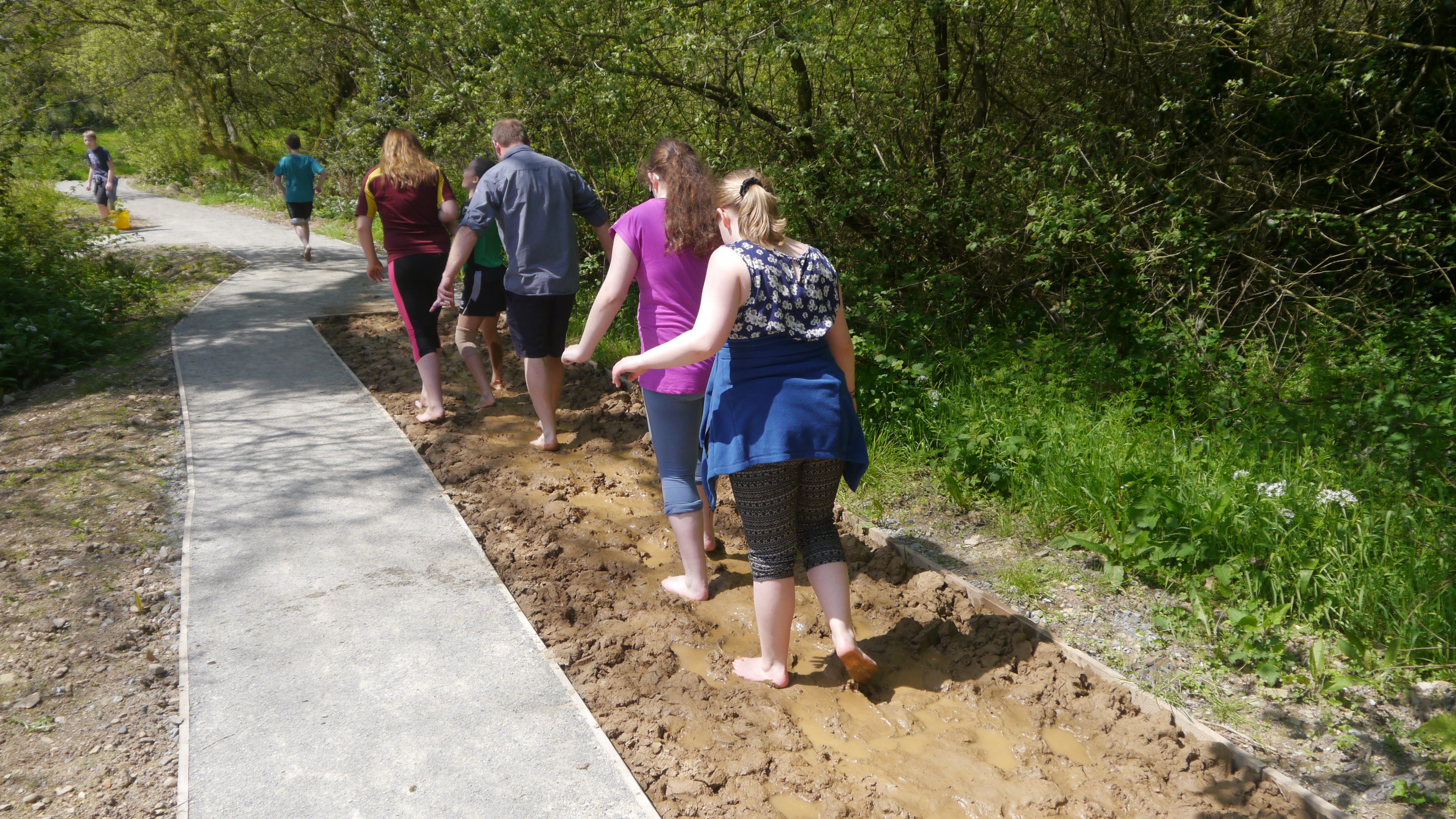 A group walking the barefoot on sand on Barefoot Trail at Castell Henllys 