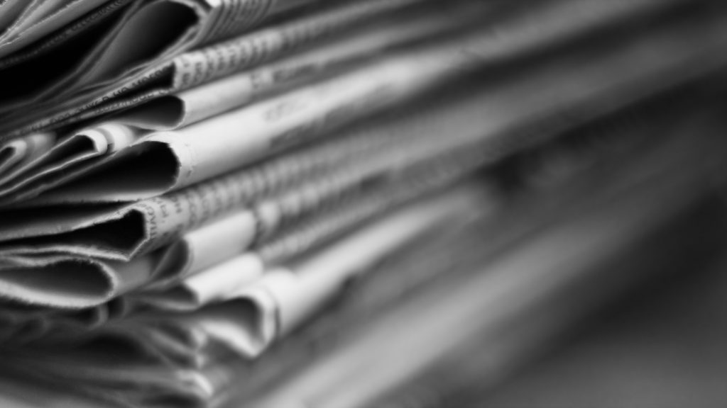 Newspapers folded and stacked in a pile. Old journals with news on wooden table. Retro style, blurred background with selective focus, close up