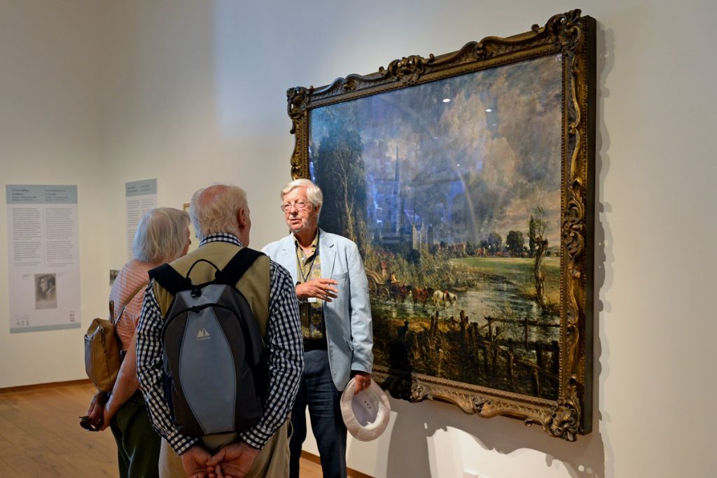 3 people standing in front of on e Constables paintings 