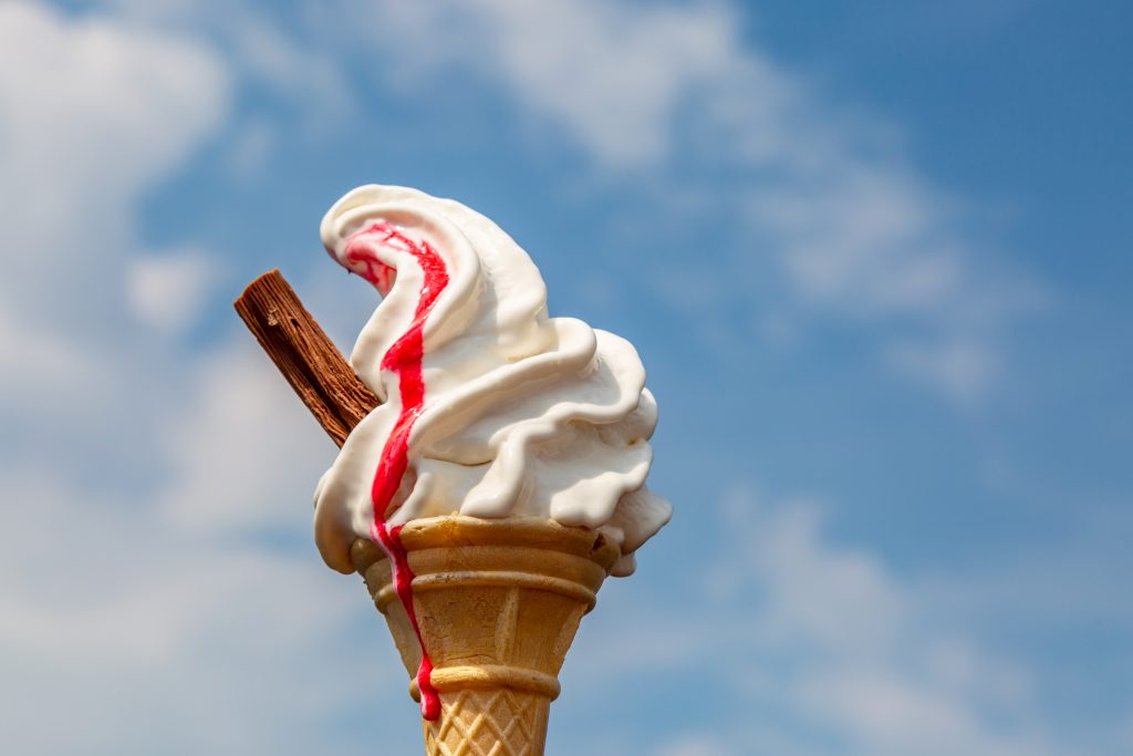 A vanilla ice cream cone with strawberry sauce, against a blue sky