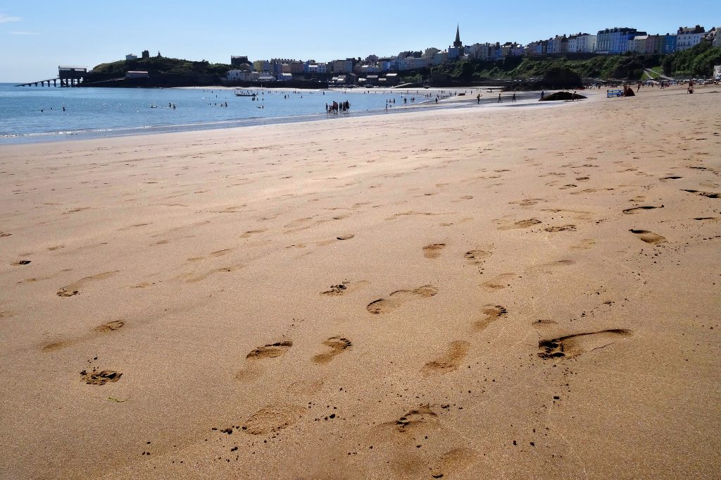 Footprints left in the sand on a beach on a sunny day with a seaside town in the background