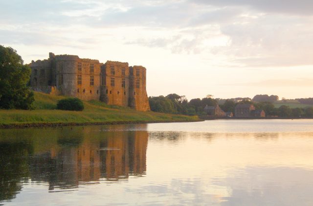 A ruined castle viewed at twilight across a calm pond