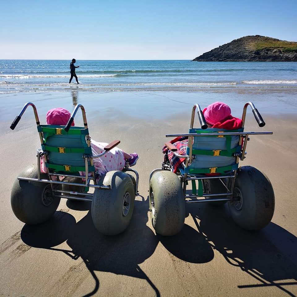 Two children on beach wheelchairs facing out to sea on a sandy beach