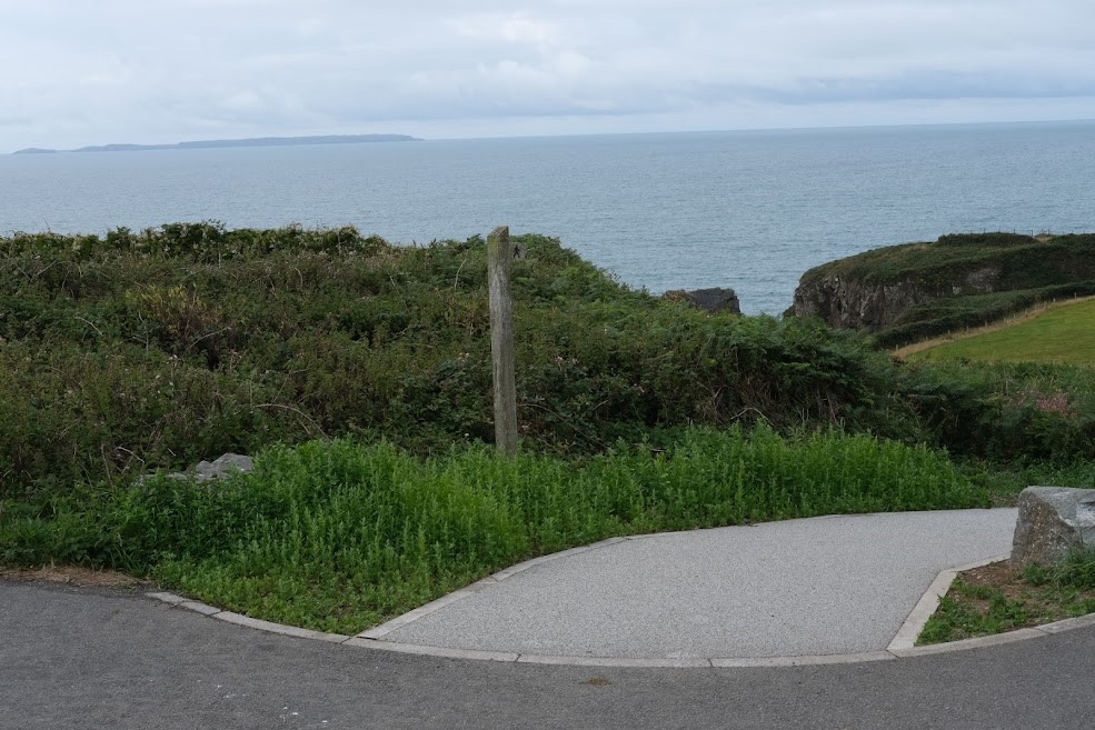 Surfaced footpath alongside grassy verge with the sea in the distance