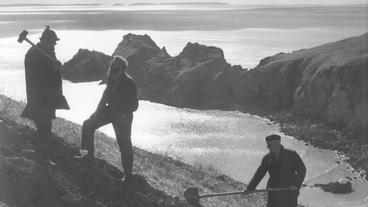 Black and white photograph from 1950s showing 3 men digging a path on a grassy clifftop