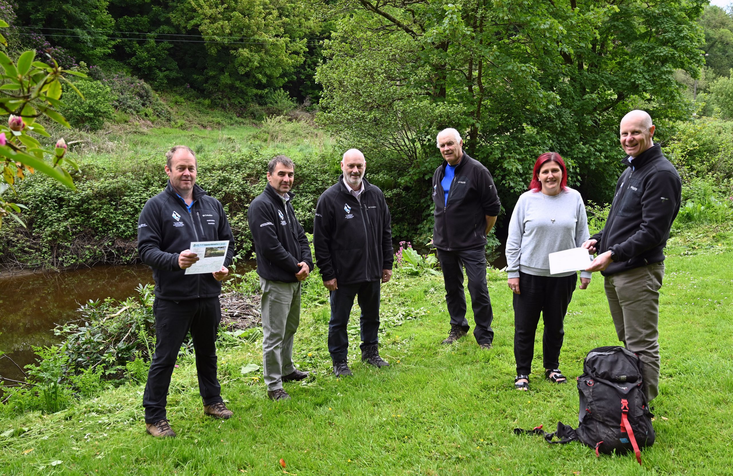 Five people standing on the grassy banks of a river looking towards the camera