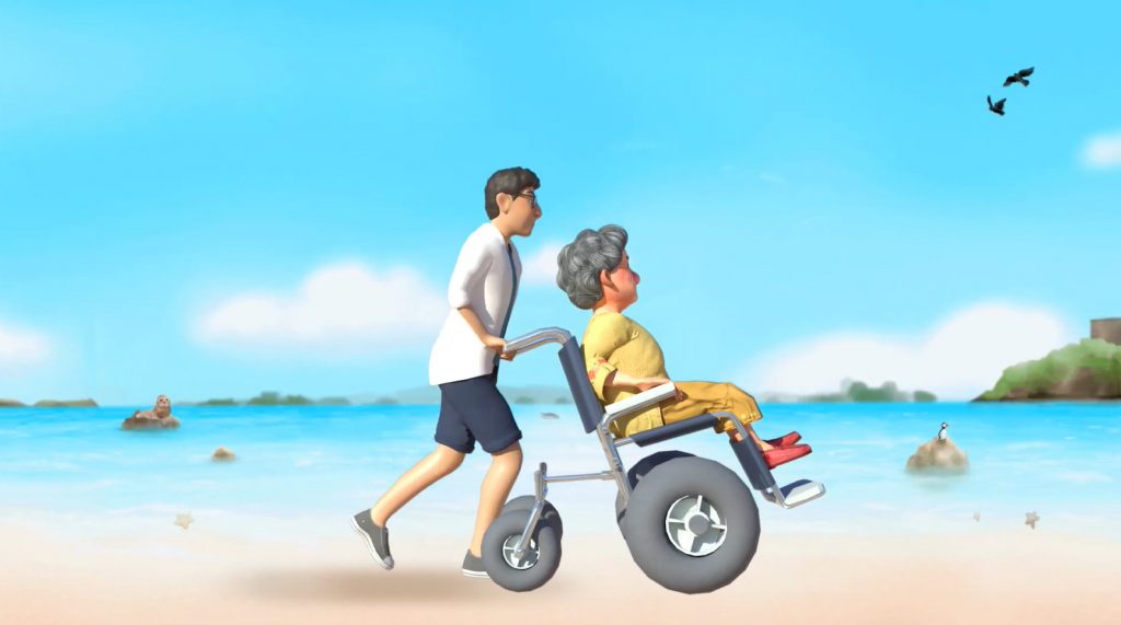 Still frame from a 3d animation depicting a woman in a beach wheelchair being pushed along a sandy beach on a sunny day