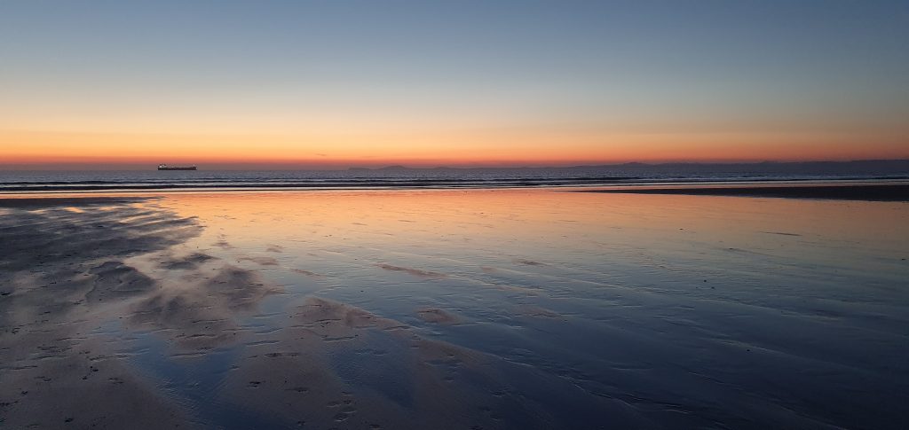 Orange and yellow colours on the horizon viewed across a sandy beach during a sunset . Location pictured is Broad Haven North, Pembrokeshire