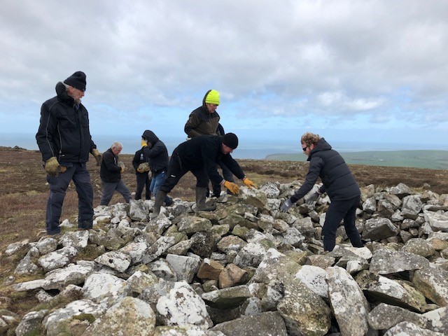 Pembrokeshire Coast National Park volunteers helping the community archaeologist and area ranger reconsolidate the shape of a protected bronze age cairn, following ongoing disturbance from visitors