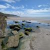 Elizabeth Fitzpatrick Newgale 2022 View across a rockpool on a sandy beach on a sunny day with a headland jutting into the sea in the background. Location Pictured is Newgale, Pembrokeshire