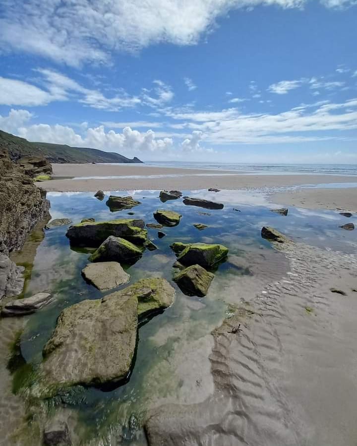 View across a rockpool on a sandy beach on a sunny day with a headland jutting into the sea in the background. Location Pictured is Newgale, Pembrokeshire