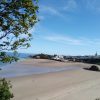 Jennifer Richards Tenby May 2020 (Lockdown) View across a sandy beach to a seaside town featuring a harbour, two lifeboat houses, colourful townhouses anda church spire towering above them. Location pictured is Tenby, Pembrokeshire