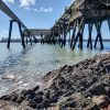 Keith South Hook 2022 View from beneath a pier structure jutting out into a body of water with pipes running along one side of the structure. location is South Hook, Pembrokeshire