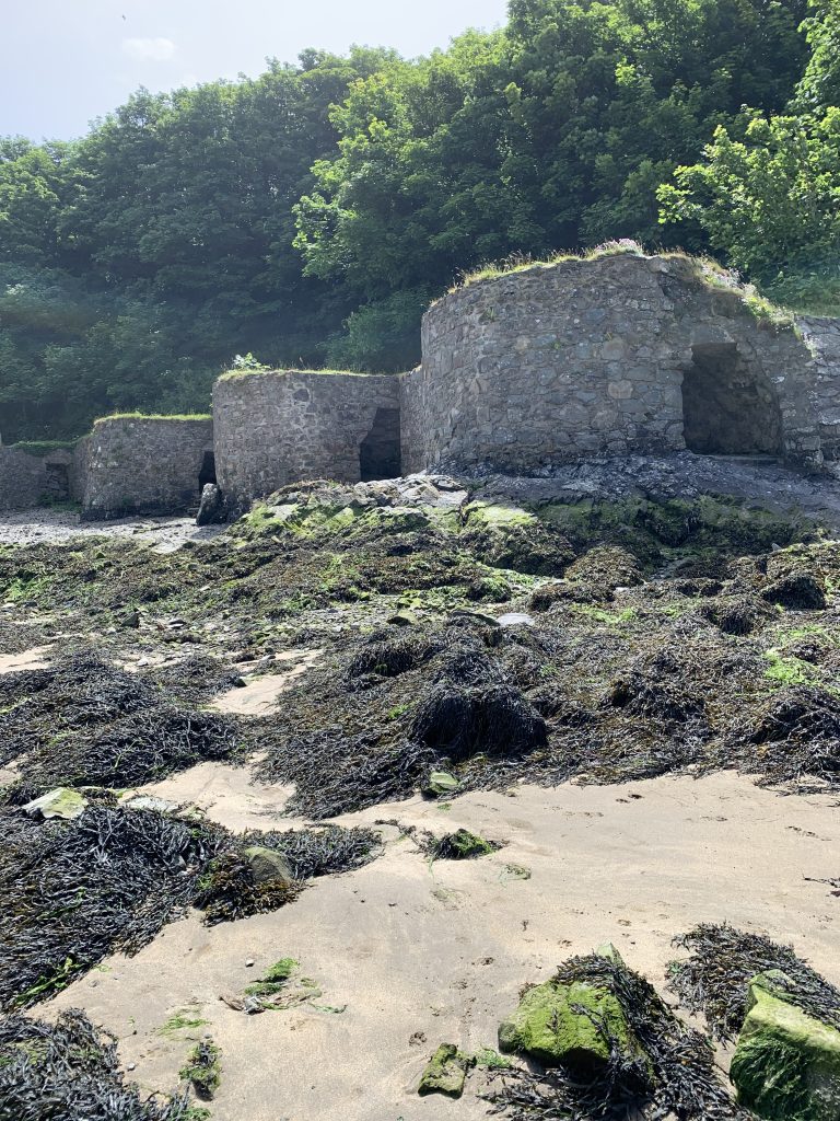 Three stone lime kilns in a sandy harbour with rocks covered with seaweed scattered across the dry seabed. Location pictured is Solva, Pembrokeshire