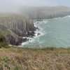 Sian Thorne Manorbier Towards Freshwater West 2022 Photograph of limestone cliffs topped with grass on a misty day with bluegreen seas crashing against the bottom of the cliffs.