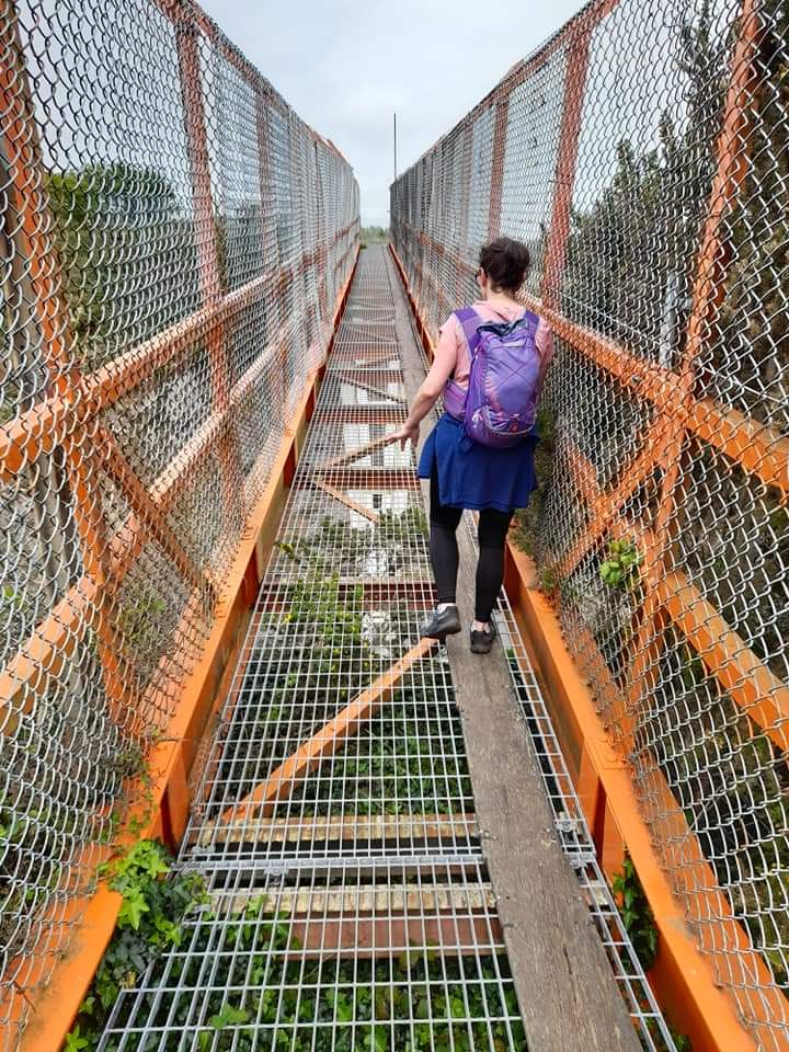 Person walking across a metal bridge enclosed on each side by a chain link fence