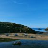 Several boats moored in a tidal harbour at low tide, leaving many of them leaning as the tide recedes leaving a sandy bed below.  It's a sunny day with clear blue skies. Location pictured is Solva, Pembrokeshire