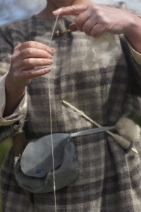 Person in Iron Age costume holding a thread of wool.