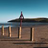 Empty sandy beach with wooden fence posts dotted along the shore on a sunny day. Location in picture is Newport Sands, Pembrokeshire