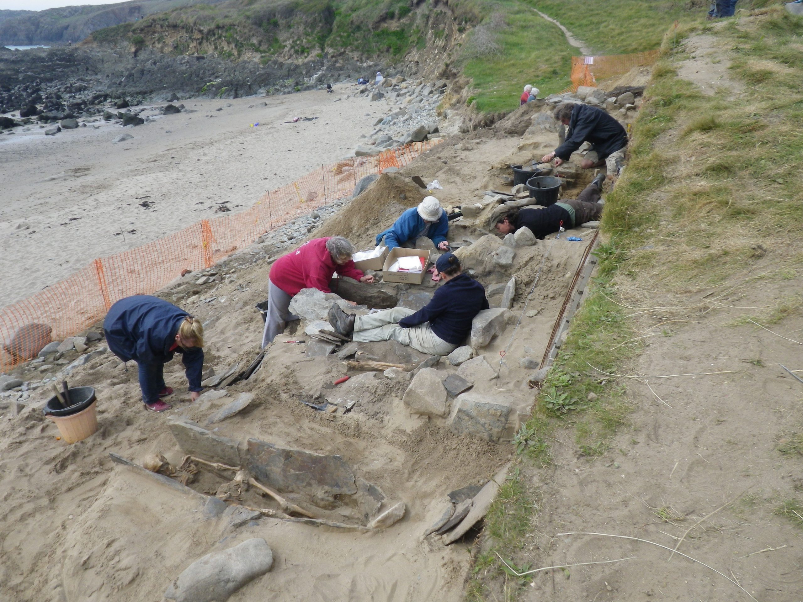 Six people excavating a site as part of an archaeological dig next to a sandy beach. Location pictured is St Patrick's Chapel, Whitesands, St Davids, Pembrokeshire