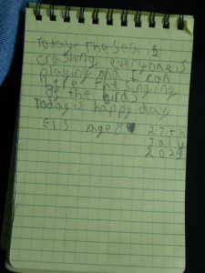 Poem written in a notebook. It reads: Today the sea is crashing everyone is playing and I can ear the singing of the birds. Today is a happy day. Eis age 8. 27th July 2023.