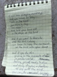 Poem written in a notebook. It reads: If you are playing monkeys and you want to say &quot;look at the bird&quot; you have to say &quot;oo-oooo&quot; and hold your hand out in the shape of the bird  And if you want to describe what the bird is doing You have the bird is doing You have to copy the movement  of the bird with your hand  and if you do this gliding in the current of air In perfect control, tensing, poised ready to dive and every finger, a feather at one with the wind, you can for a moment, become the bird