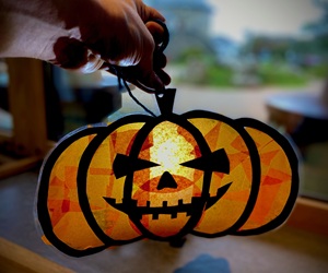 Image of a hand holding a homemade pumpkin shaped suncatcher