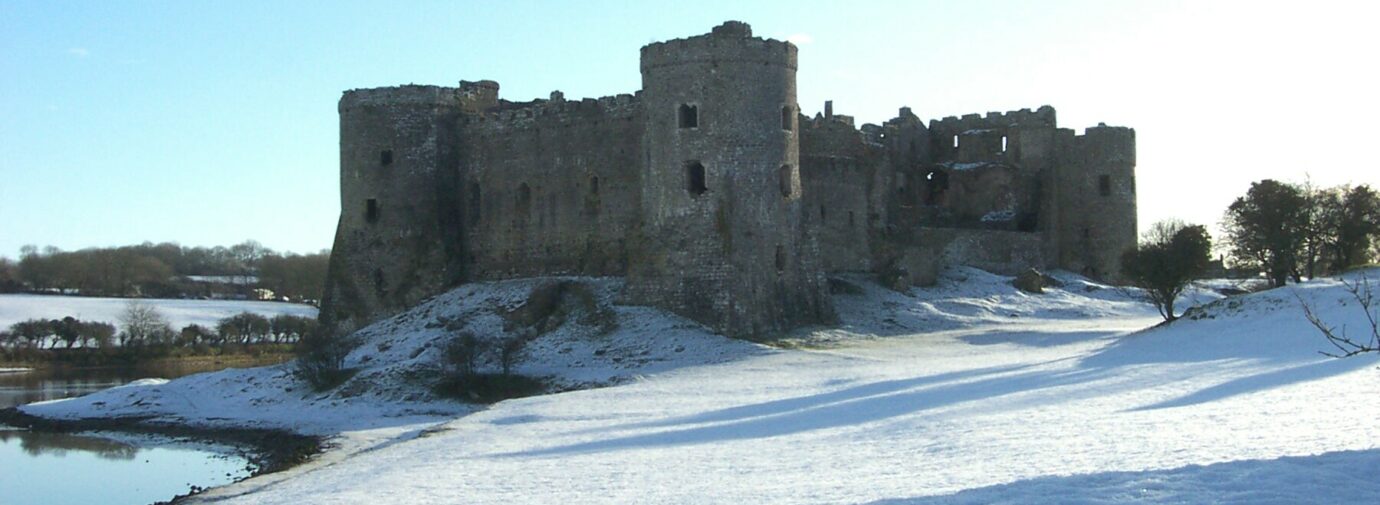 Large stone castle on a mound covered in snow, with a body of water to the left.
