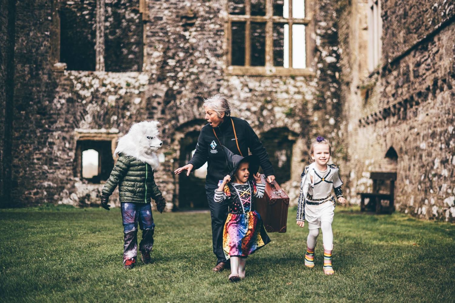 A member of Castle staff roams the grounds of Carew Castle with three young children dressed in Halloween costumes.